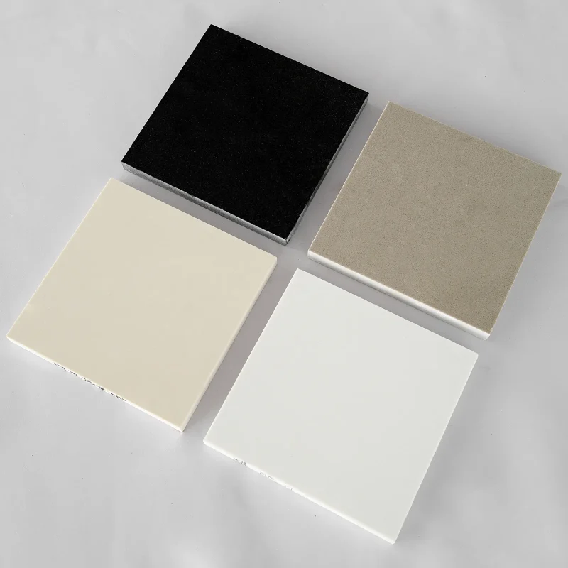 Black, taupe, cream and white solid color quartz slab samples arranged at an angle on a grey surface
